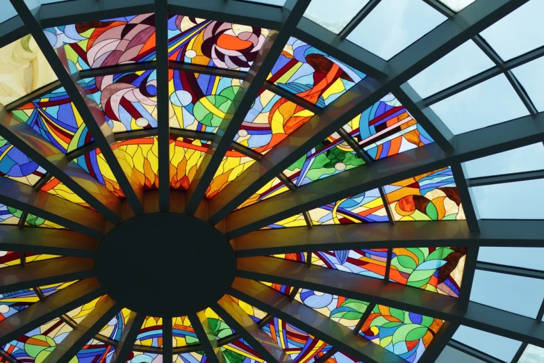 a circular stained glass window in a building, a mosaic, inspired by Abraham van den Tempel, art nouveau, sunny sky light, explosion of colors, inside a glass box, contemporary art