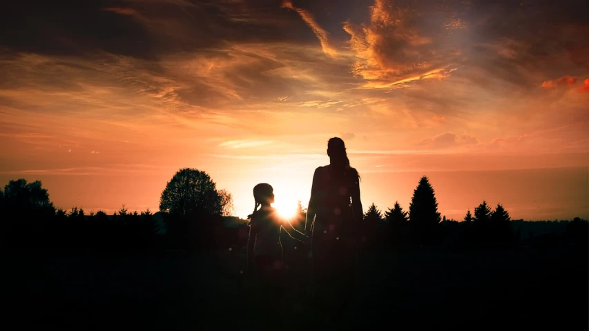 a couple of people that are standing in the grass, a picture, by Eugeniusz Zak, pexels, symbolism, backlight sunset sky, mother, of a family standing in a park, with a kid