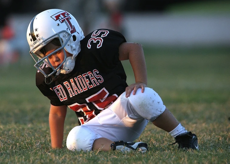 a young football player sitting on the ground, by Paul Davis, pixabay, with a hurt expression, photograph credit: ap, raider, 2009