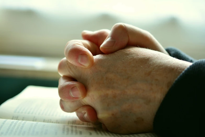 a close up of a person holding a book, unilalianism, prayer hands, istockphoto, sitting with wrists together, warts