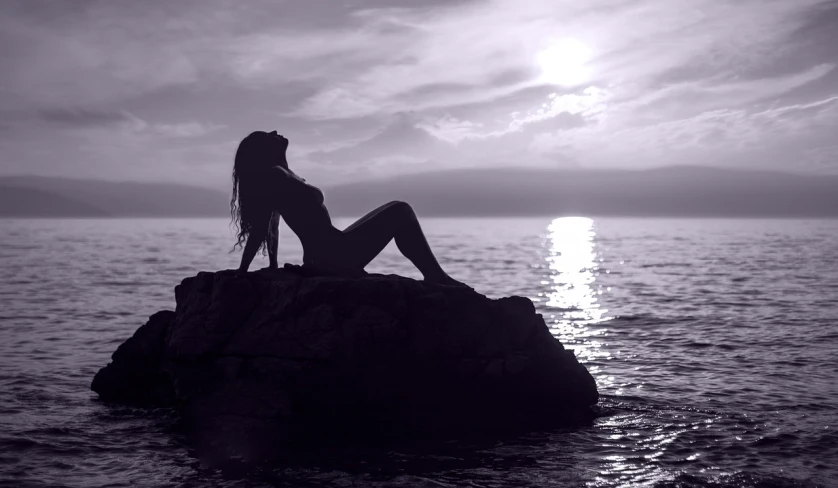 a woman sitting on top of a rock in the water, a black and white photo, romanticism, at purple sunset, beautiful sexy woman photo