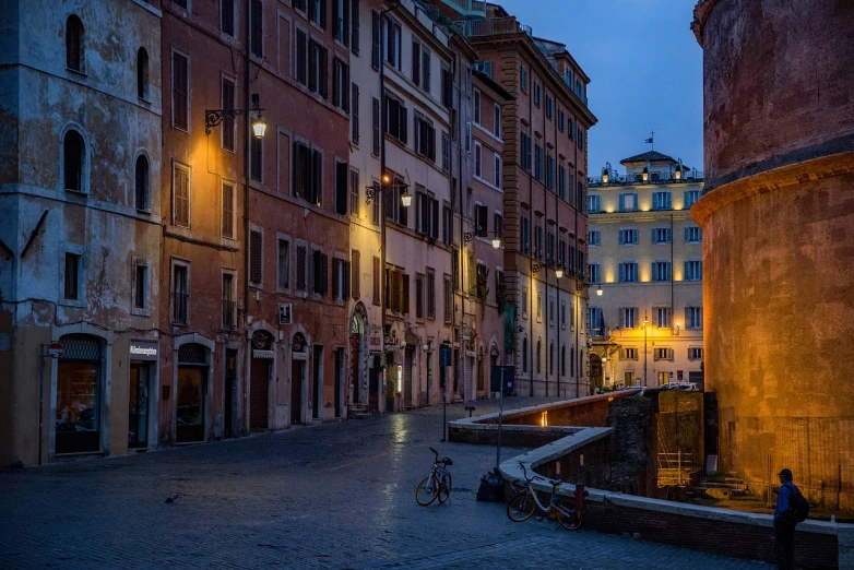 a couple of people walking down a street next to tall buildings, by Carlo Maderna, pexels contest winner, realism, nightfall. quiet, ancient roman setting, in a square, contraposto