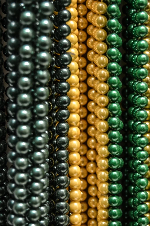 a close up of a bunch of beads, by Karel Štěch, pexels, renaissance, gradient black green gold, gold and pearl necklaces, in a row, hong kong