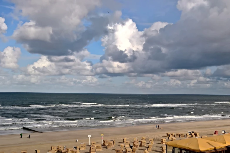 a group of umbrellas sitting on top of a sandy beach, a picture, renaissance, huge clouds, boardwalk, view from high, shot on webcam