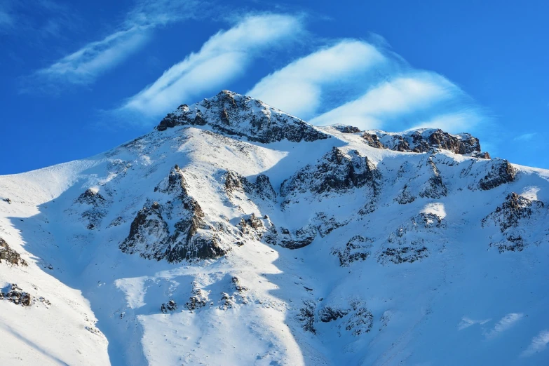 a man riding a snowboard down the side of a snow covered mountain, a tilt shift photo, by Cedric Peyravernay, shutterstock, cirrus clouds, with snow on its peak, the photo shows a large, large rocky mountain
