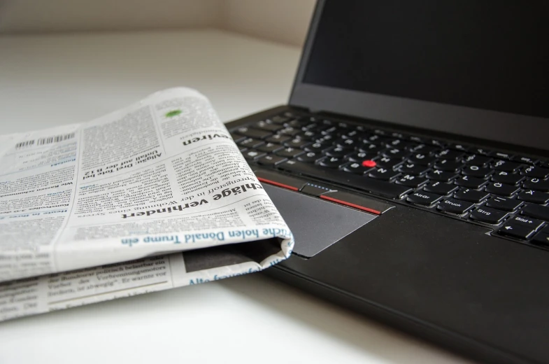 a laptop computer sitting on top of a desk next to a newspaper, by Carey Morris, pixabay, private press, thinkpad, view from the bottom, looking to the right, medium closeup shot