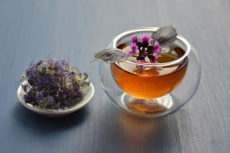 a cup of tea next to a small bowl of flowers, by Rhea Carmi, pexels, renaissance, purple liquid in cup glowing, basil leaves instead of leaves, molecular gastronomy, motivational