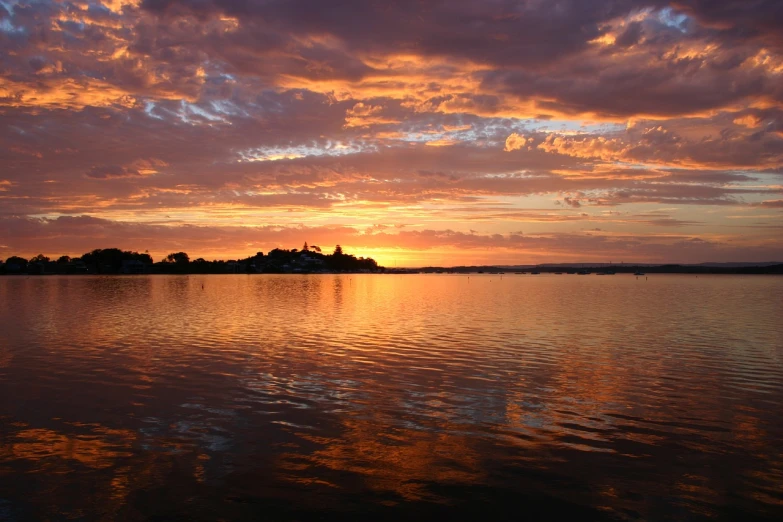 a large body of water with a sunset in the background, a picture, by Linda Sutton, flickr, hurufiyya, picturesque, prizewinning, orange clouds, an island