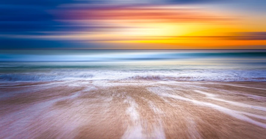 a large body of water sitting on top of a sandy beach, a pastel, by Etienne Delessert, shutterstock, massive motion blur, colorful sunset!!, cornwall, an abstract tropical landscape