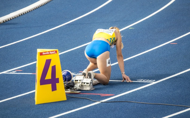 a woman that is kneeling down on a track, by Dietmar Damerau, synchromism, ukrainian flag on the left side, sport bra and shorts, blonde swedish woman, very sharp photo