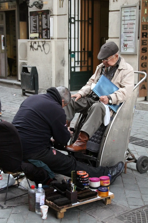 a man sitting on top of a chair next to another man, by Luis Molinari, street art, focus on his foot, old man doing hard work, makeup, madrid