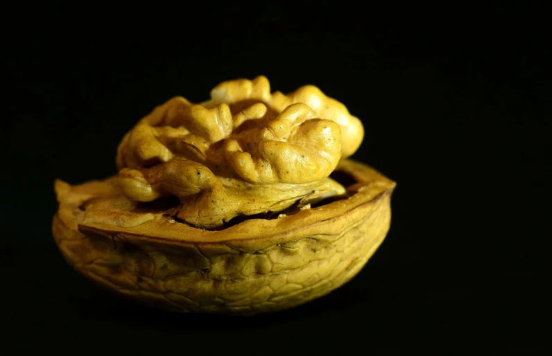 a walnut in a walnut shell on a black background, by Cheng Zhengkui, hurufiyya, miniature product photo, yellowed, baroque object, close-up product photo