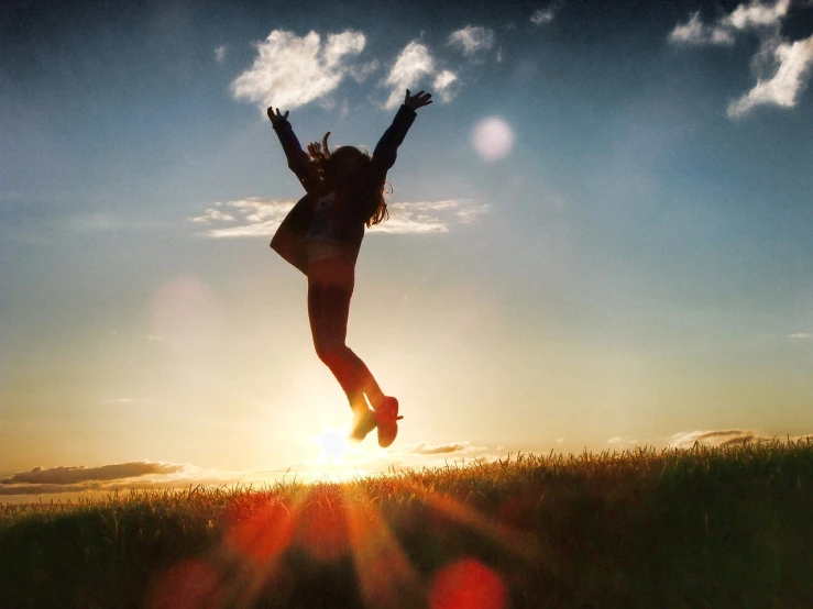 a person jumping in the air in a field, a picture, happening, sunburst behind woman, happy smiling, triumphantly, high detalied