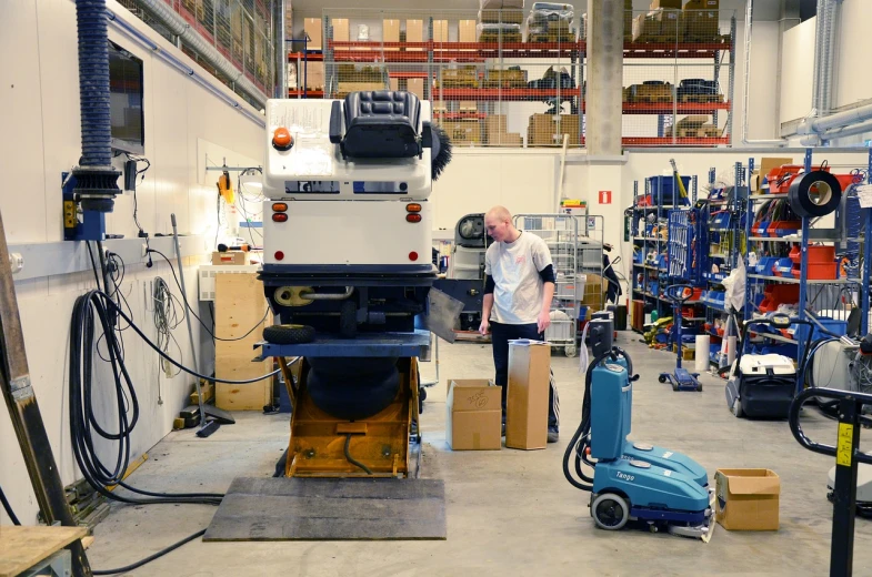 a man standing next to a machine in a warehouse, by Jakob Gauermann, credit esa, majestic sweeping action, giant athanor, kneeling at the shiny floor