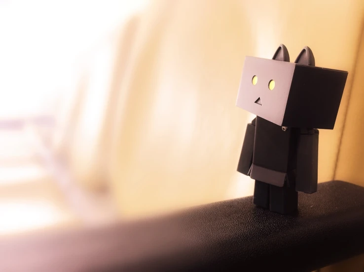 a small black and white robot sitting on top of a table, a picture, tumblr, digital art, no blur dof bokeh, sad cat, papercraft, blocky
