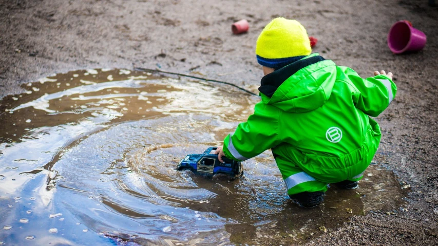 a small child playing in a puddle of water, by Anato Finnstark, pexels, wearing green clothing, toy photo, construction, cold as ice! 🧊