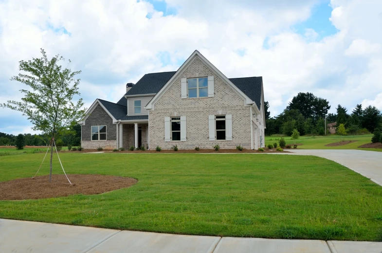 a house sitting on top of a lush green field, by John Luke, shutterstock, driveway, front elevation, brick, residential design