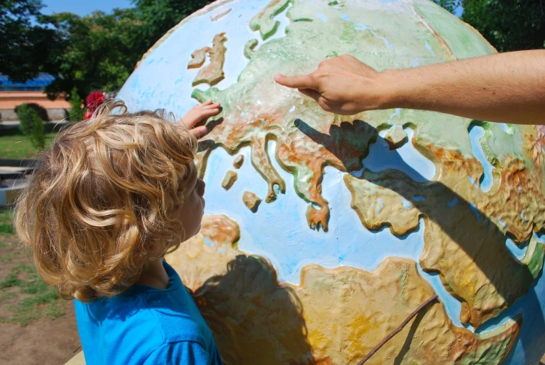 a little boy that is standing in front of a globe, by Erwin Bowien, pexels, interactive art, map of europe, large bubble archaeologies, closeup photo, on a sunny day