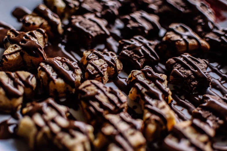 a white plate topped with chocolate covered cookies, a tilt shift photo, by Alexander Bogen, pexels, baroque, in rows, made of glazed, cell bars, full res