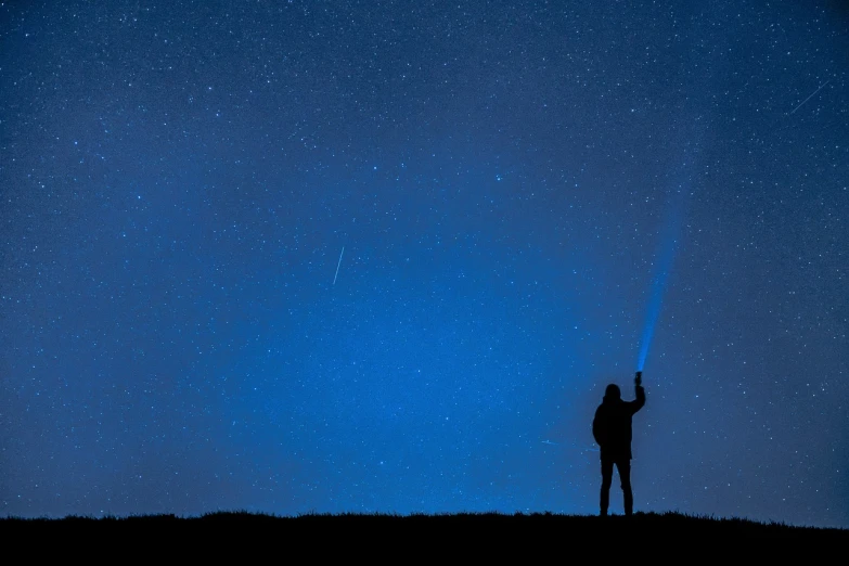 a person standing on top of a hill under a sky full of stars, by Zoran Mušič, shooting star, blue atmosphere, silhouettes in field behind, cell phone photo