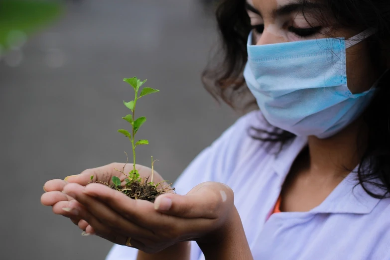 a woman wearing a face mask holding a plant, by Ramón Silva, pixabay, with a lab coat, seedlings, 30-year-old woman from cuba, air pollution