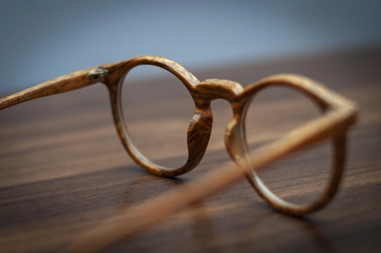 a pair of glasses sitting on top of a wooden table, by Maksimilijan Vanka, unsplash, photorealism, side view intricate details, wooden frame, commercial product photography, in style of monkeybone