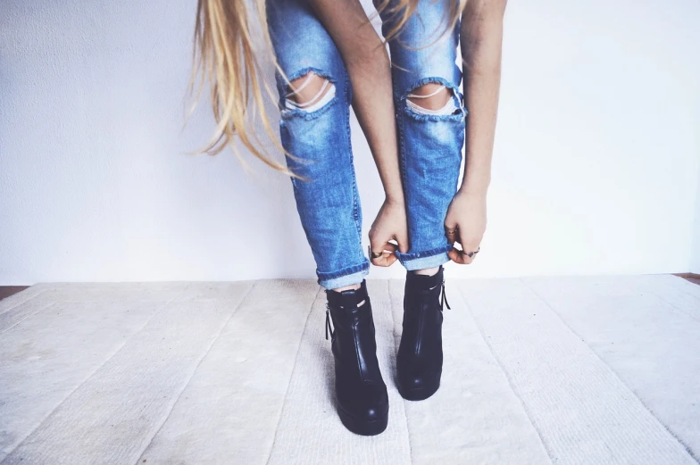 a woman standing on top of a wooden floor, tumblr, jeans and black boots, laced, half image, beautiful blonde girl