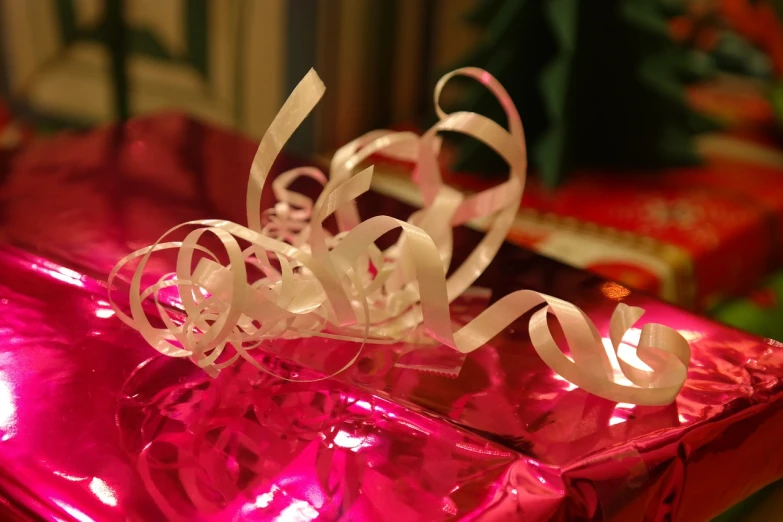 a pink present sitting on top of a table, by Alice Mason, swirly curls, closeup - view, red and white lighting, white ribbon