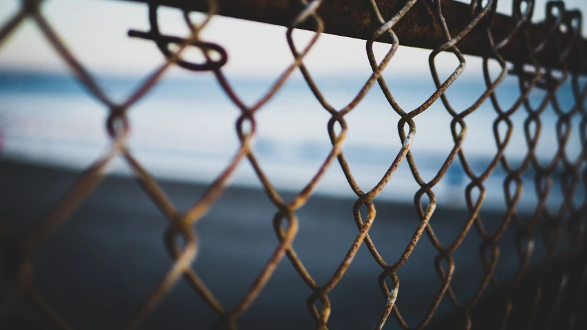 a chain link fence with the ocean in the background, a picture, unsplash, 4 k vertical wallpaper, rust background, shot on nikon z9, grungy