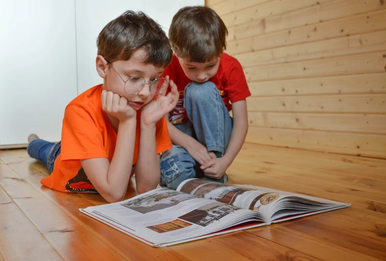 two young boys sitting on the floor reading a book, a picture, by Maksimilijan Vanka, pixabay, reading glasses, photorealistic magazine picture, stock photo, wooden desks with books