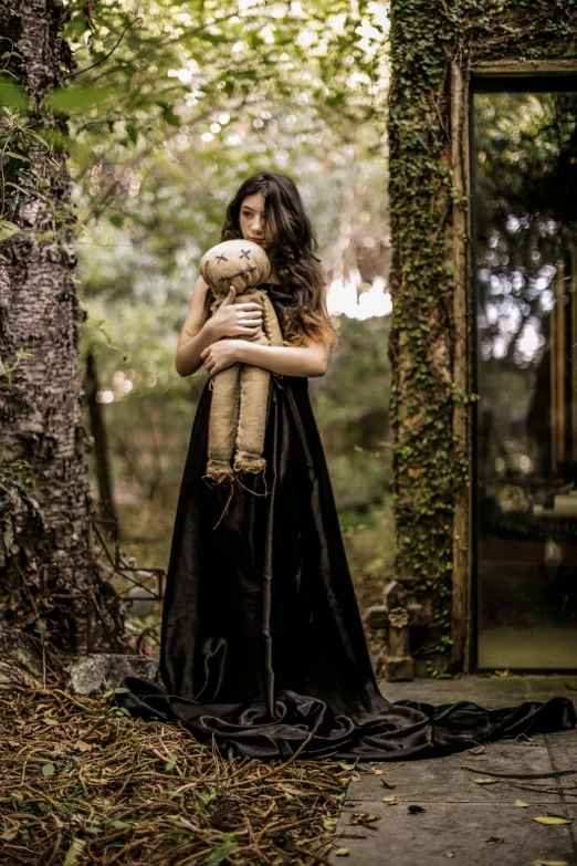 a woman in a black dress holding a teddy bear, by Lucia Peka, unsplash, surrealism, brad kunkle elson peter, embrace porcelain doll, long raven hair, in a garden