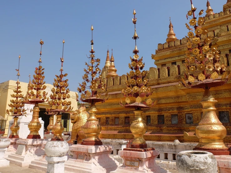 a group of golden statues in front of a building, a picture, myanmar, ornate spikes, beautiful day, side view from afar