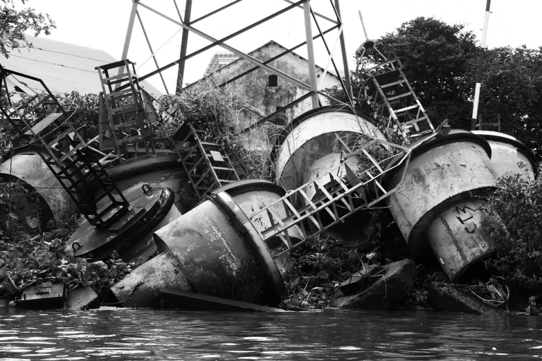 a boat sitting on top of a river next to a forest, by Arthur Sarkissian, flickr, process art, 9 steel barrels in a graveyard, kowloon walled city, collapsed brutalist architecture, bw photo