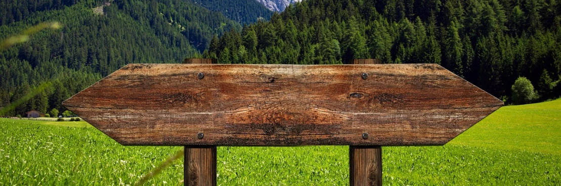 a wooden sign sitting on top of a lush green field, trending on pixabay, folk art, background image, mountainous background, wood chair, billboard image