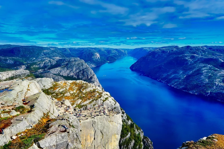 a large body of water surrounded by mountains, by Armin Hansen, pexels, romanticism, vibrant blue, norwegian landscape, looking down a cliff, city of pristine colors