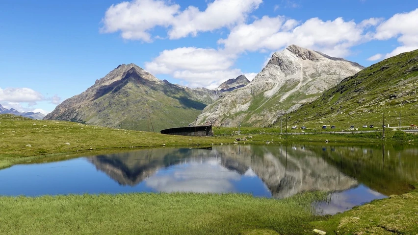 a body of water sitting on top of a lush green hillside, by Werner Andermatt, les nabis, alpine architecture, marvellous reflection of the sky, adrien girod, family friendly