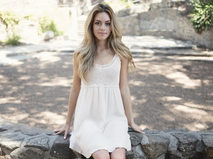 a woman in a white dress sitting on a stone wall, sydney sweeney, simple cream dress, half - length photo, full res