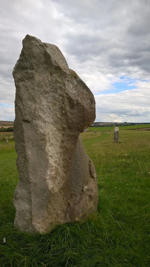 a large rock sitting on top of a lush green field, a portrait, by Joseph Henderson, flickr, land art, neolithic standing stones, close-up shot from behind, pillar, selfie shot straight on angle