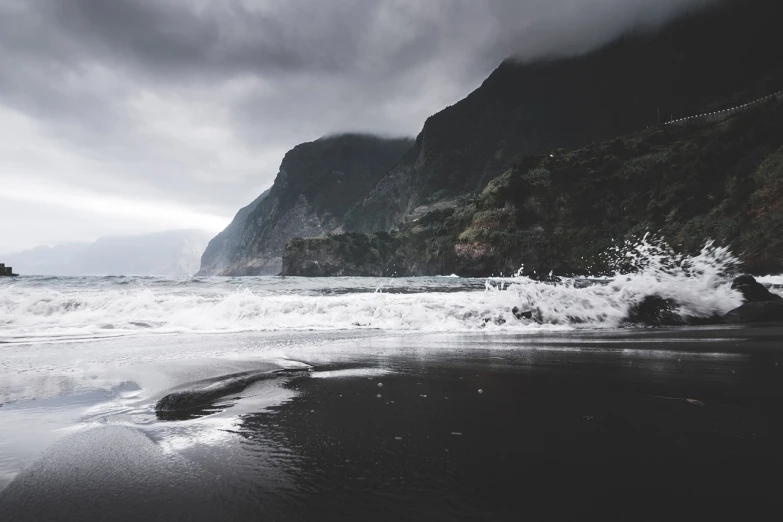 a man riding a surfboard on top of a sandy beach, a picture, by Lucas Vorsterman, unsplash contest winner, realism, sea storm and big waves cliffs, azores, old photo of a creepy landscape, black sand