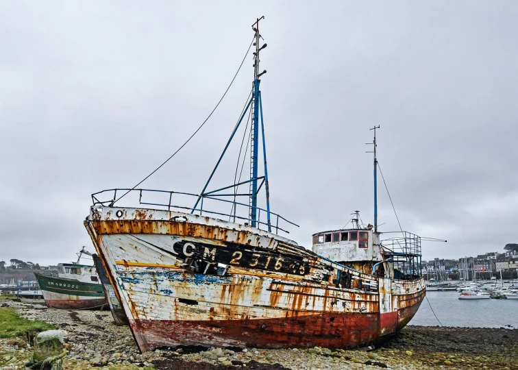 a rusty boat sitting on top of a beach next to a body of water, a portrait, by Richard Carline, flickr, ships in the harbor, coloured, grey, christopher alexander