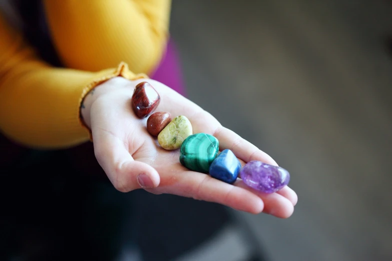 a person holding a handful of stones in their hand, colorful crystals, the woman holds more toys, five fingers on the hand, a close up shot