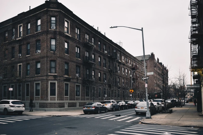 a group of cars driving down a street next to tall buildings, a photo, inspired by Thomas Struth, pexels, harlem renaissance, location of a dark old house, long shot wide shot full shot, street corner, schomburg