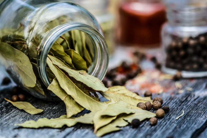 a jar filled with leaves sitting on top of a wooden table, a picture, renaissance, spices, close-up product photo, broken composition, pepper