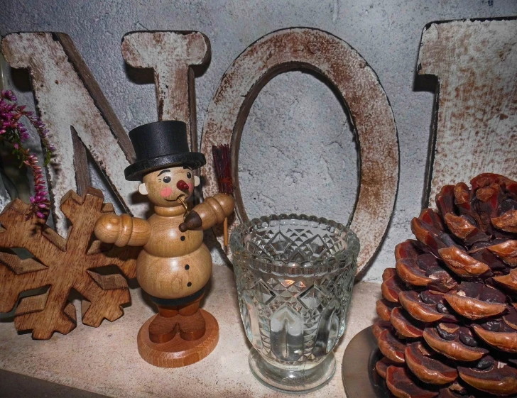 a wooden snowman sitting on top of a table next to a glass, folk art, oh no, old english, nut, shelf