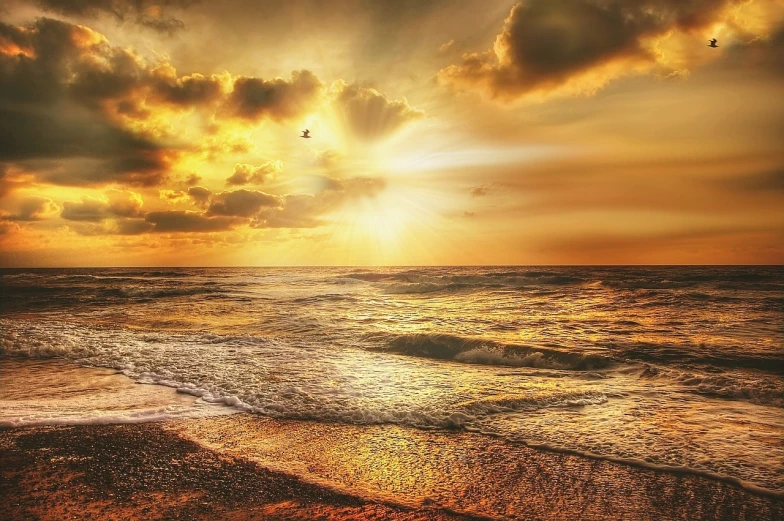 a sunset over the ocean with birds flying in the sky, a picture, fine art, golden heavenly lights, which shows a beach at sunset, enhanced photo, clouds and waves