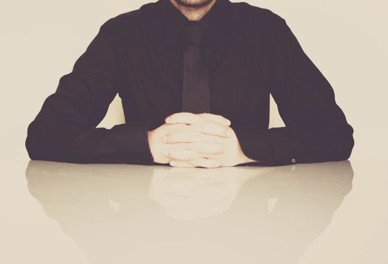 a man in a black shirt and tie sitting at a table, minimalism, retro effect, very sharp photo