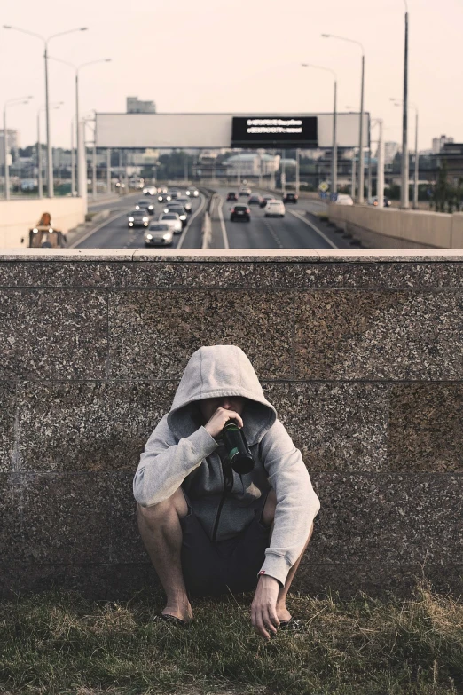 a man sitting on the side of a road holding a camera, unsplash, street art, distant hooded figures, overpass, hood covers his eyes, aleksander rostov