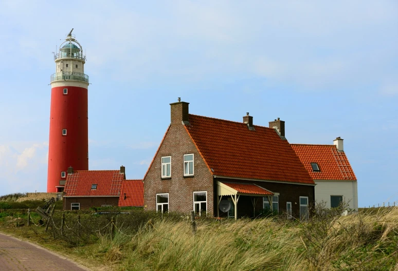 a red and white lighthouse sitting on the side of a road, by Jan Tengnagel, village house, dune, brick, tourist photo