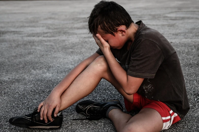 a boy sitting on the ground with his head in his hands, pixabay, realism, tony hawk crying, on a parking lot, teen girl, tears running down