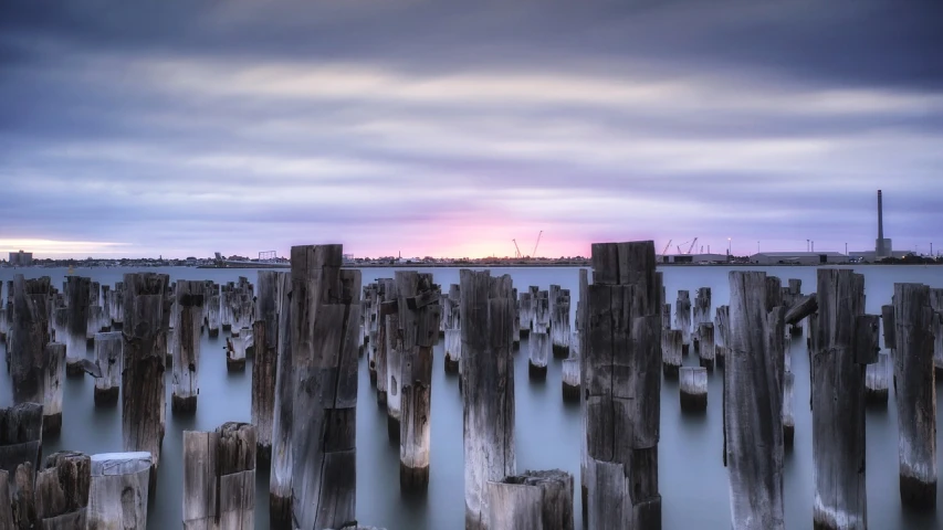 a bunch of wooden poles sticking out of the water, a tilt shift photo, inspired by George Pirie, at purple sunset, concrete pillars, melbourne, slow exposure hdr 8 k